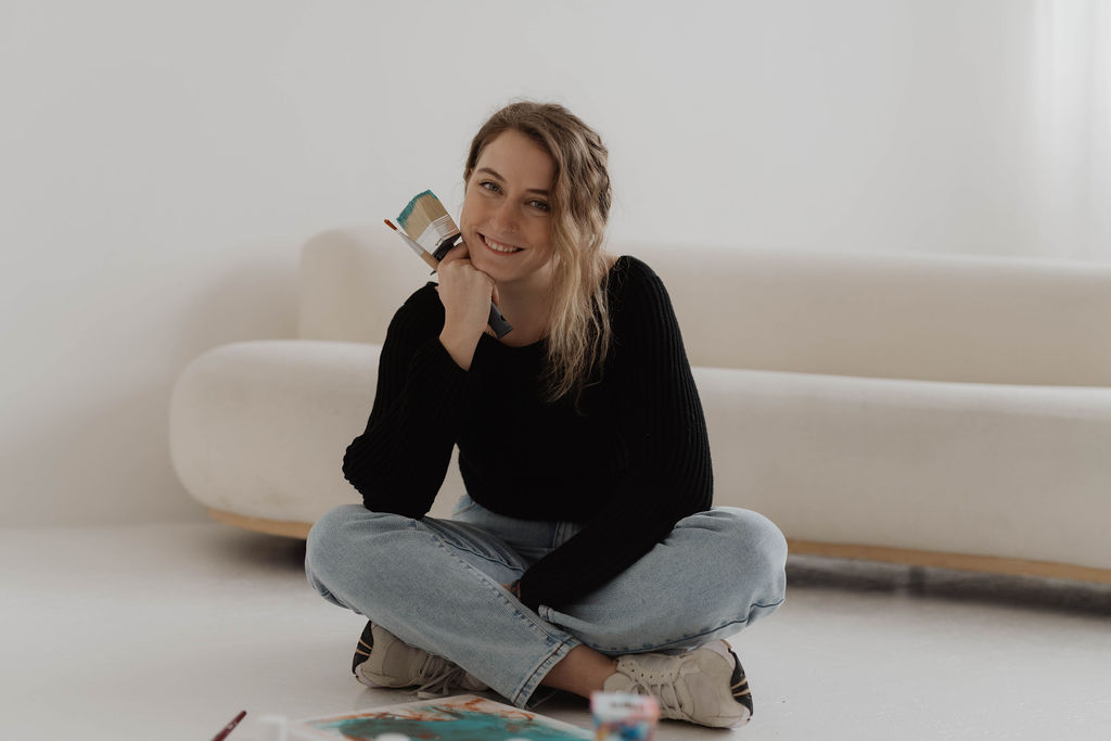 Laura im Studio, sitzt am Boden mit Pinsel und Farben